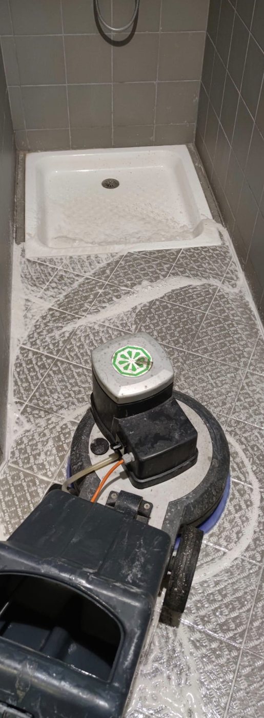 Machine de nettoyage sur le sol carrelé d’une salle de bain, devant le receveur de douche